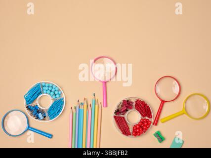 Verschiedene Büro- und Schulmaterialien, darunter Bleistifte, Lupen, Büroklammern und Pins, sind auf einem neutralen Hintergrund ordentlich angeordnet. Stockfoto