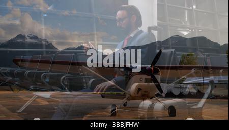 Sitzender Geschäftsmann im Marineblau, der Smartphone in der Flughafenlounge überprüft, mit Requisitionsflugzeug, Kopierraum Stockfoto