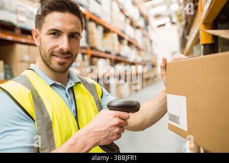 Stehender männlicher Lagerarbeiter, der eine Sicherheitsweste im Gang trägt, mit Handscanner Stockfoto