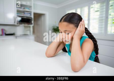 Denkendes junges Mädchen, das auf der Kücheninsel Hände an die Ohren drückt, mit Pflanzen und Kochbüchern, Kopierraum Stockfoto