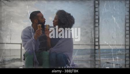 Romantisches Paar tauscht Eiskegel an der Strandpromenade mit violetter Decke aus Stockfoto