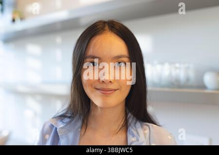 Posierende asiatische Frau mit Polka Dot-Shirt, die in der Küche steht, mit Metallregalen, Gläsern, Schüsseln Stockfoto
