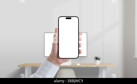 Smartphone mit leerem weißen Bildschirm in der Hand in einem modernen Büro, Desktop-Computer im Hintergrund, perfekt für Mockup der mobilen Benutzeroberfläche Stockfoto