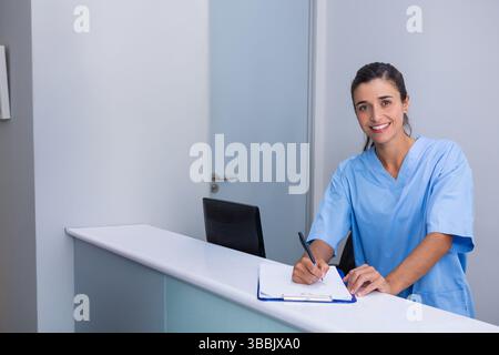 Schreibende Krankenschwester, die an der Rezeption in der Klinik steht, Klemmbrett und Stift hält, Kopierraum Stockfoto