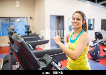 Lächelnde Frau joggt auf dem Laufband in einem modernen Fitnessstudio mit Fahrrädern, Kopierraum Stockfoto