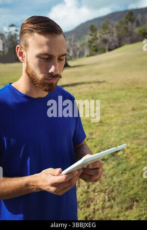 Ein bärtiger Mann steht auf offenem Grasfeld und hält eine weiße Tablette unter teilweise bewölktem Himmel Stockfoto