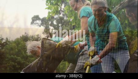 Bild von Gras über älteren kaukasischen Männern und jungen Frauen, die Müll im Wald sammeln Stockfoto