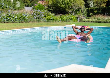 Entspannender afroamerikanischer Mann, der auf einem aufblasbaren Ring im Pool schwimmt, Sonnenbrille trägt, Kopierraum Stockfoto