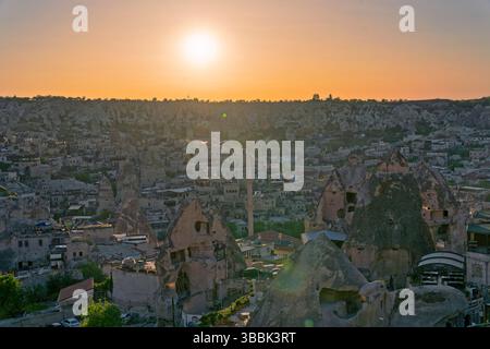 Die Sonne untergeht über einer Stadt und verstreuten Felsformationen in Kappadokiens Goreme und taucht die Landschaft in warmes goldenes Licht. Stockfoto