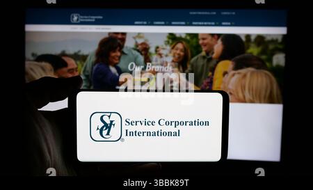 Stuttgart, Deutschland - 01-07-2024: Person mit Mobiltelefon mit Logo der US-amerikanischen Bestattungsgesellschaft Service Corporation International auf dem Bildschirm Stockfoto