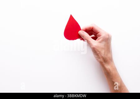 Eine weibliche Hand, die einen Papiertropfen Blut auf weißem Hintergrund und Kopierraum hält. Stockfoto