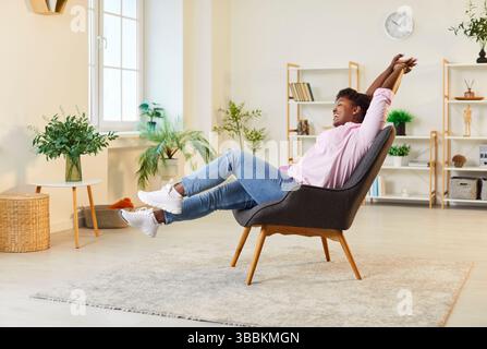 Glückliche afroamerikanische Frau, die sich im Sessel entspannt und sich ausdehnt Stockfoto