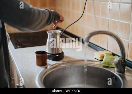 Mann, der ein heißes Getränk mit einem Metallkessel in einer gemütlichen Küche zubereitet Stockfoto