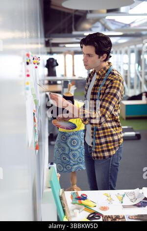 Ein Mann in den Zwanzigern, der Skizzen auf Studioblatten anordnet, mit Stoffmustern Stockfoto