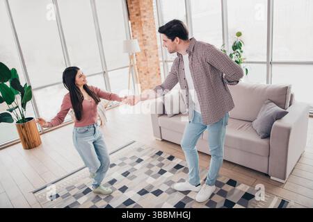 Junges Paar tanzt fröhlich zusammen in einem sonnigen Wohnzimmer, genießt Freizeit und verbindet sich in einer ungezwungenen und entspannten Atmosphäre zu Hause. Stockfoto