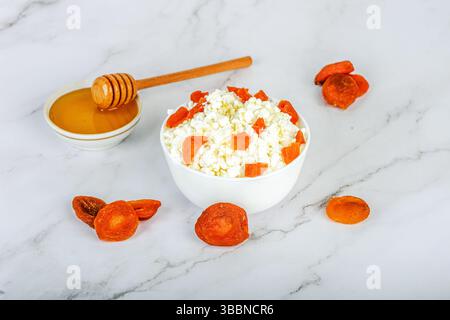 Frischer Hüttenkäse mit getrockneten Aprikosen und Honig in einer weißen Schüssel und Zutaten rund um die Schüssel. Gesunde Ernährung. Stockfoto