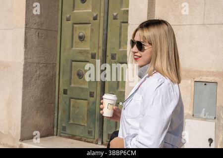 Selbstbewusster Arzt, der außerhalb des Krankenhauses eine Kaffeepause genießt und Gesundheitsfachkräfte und ihr Engagement vertritt Stockfoto