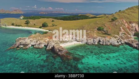 Aus der Vogelperspektive des kristallklaren türkisfarbenen Wassers, das sanft über die felsige Küste einer malerischen Insel im Komodo-Nationalpark in Indonesien spült, zeigt die raue Schönheit der Natur Stockfoto