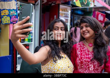 Zwei junge Frauen posieren für ein Selfie-Foto auf dem Crosded Market während des Durg Puja Festivals in Kalkutta, Westbengalen, Indien Stockfoto