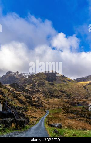 Eine gewundene Asphaltstraße durch das Gletschertal von Cwm Idwal führt zu zerklüfteten Snowdonia-Gipfeln unter einer dynamischen Wolkenlandschaft Stockfoto