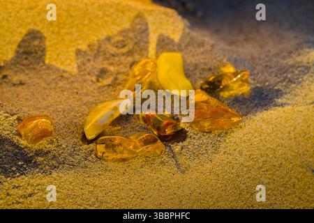 Ein Sommersonnenuntergang in Kołobrzeg erleuchtet Bernsteinsteine, die auf Sand liegen und in goldener Stunde warm glühen. Stockfoto