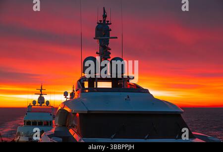 Transport großer Motoryachten über den Ozean bei Sonnenuntergang mit rotem Himmel. Stockfoto
