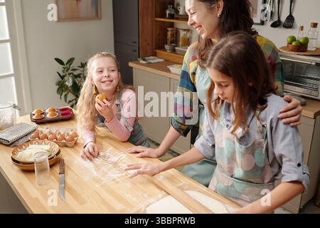 Mutter und ihre beiden Töchter backen zusammen in einer gemütlichen Küche voller natürlichem Licht und Wärme Stockfoto