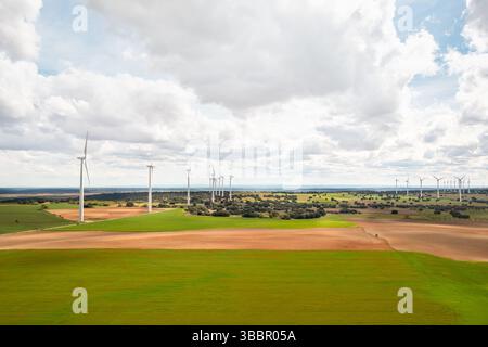 Luftaufnahme eines riesigen Solar- und Windenergieparks, der sich über grüne und rote Ackerflächen unter hellem bewölktem Himmel erstreckt und saubere Energie, Nachhaltigkeit und ökologische Innovation symbolisiert Stockfoto