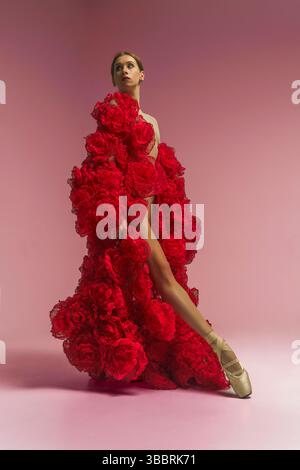 Eine junge weibliche Ballerina in einem Fotostudio in einem cape Kleid aus Rosenblumen zeigt Ballettbewegungen Stockfoto