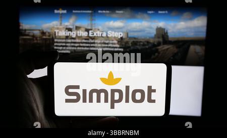 In dieser Abbildung hält eine Person ein Handy mit dem Logo der US-amerikanischen Agribusiness J. R. Simplot Company auf dem Bildschirm vor der Webseite. Stockfoto