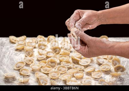 Hände, Ravioli, Fleischfüllung. Frau, die fleischige Ravioli macht. Der Koch kocht handgemachte Tortellini-Ravioli auf dem Tisch mit Mehl Stockfoto