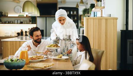 Muslime, Eltern und Kind mit Essen im Haus für Eid-Mittagessen, gesunde Mahlzeit und Festmahl zum Feiern. Mutter, Servieren und Familiengericht für die Ernährung Stockfoto