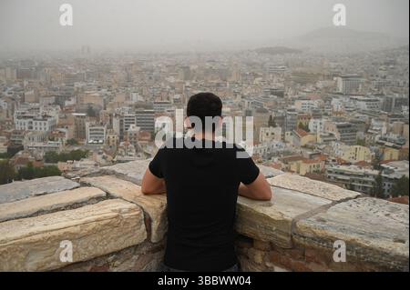 Athen, Griechenland, 16. Mai 2025. Ein Besucher blickt über die Stadt, während Athen von Staubwolken bedeckt ist. Eine dicke Decke aus Sahara-Staub fegte am Freitag über die griechische Hauptstadt und ließ die Stadt trüben und warnte die Behörden. Quelle: Dimitris Aspiotis/Alamy Live News Stockfoto