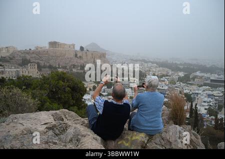 Athen, Griechenland, 16. Mai 2025. Besucher machen Fotos von der antiken Akropolis, während Athen mit Staubwolken bedeckt ist. Eine dicke Decke aus Sahara-Staub fegte am Freitag über die griechische Hauptstadt und ließ die Stadt trüben und warnte die Behörden. Quelle: Dimitris Aspiotis/Alamy Stockfoto