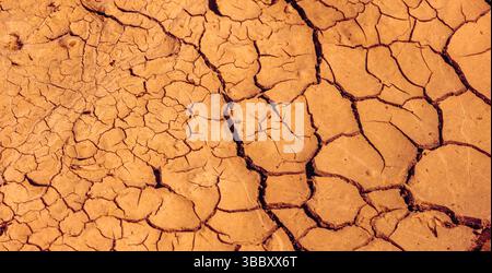 Geplatzte Erde. Eine trockene Landschaft mit zerrissenen, trockenen Erdmustern in einem warmen Orangenton Stockfoto