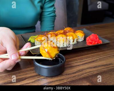 Hand halten Gourmet gebackene Sushi Rolls mit Sauce, Chili Threads, Ingwer Wasabi auf schwarzer Platte. Japanische heiß gebackene Sushi Rolls. Hochwertige Fotos Stockfoto