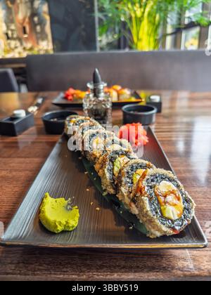 Tempura Maki Roll serviert mit hellem Wasabi und rosa Ingwer auf modernem schwarzen Teller. Crunchy Fried Sushi Roll mit Avocado Füllung auf eleganter schwarzer Platte Stockfoto