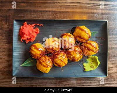 Top-down-Ansicht des gebackenen Sushi-Sets: Brötchen mit Sauce, Chili-Garnish, Ingwer, Wasabi. Asiatische Fusion: Gebackene Sushi-Rolls mit herzhaftem Topping, serviert mit Gin Stockfoto
