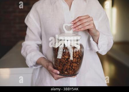 Nahaufnahme einer Frauenhände, die ein dekoratives Glas mit Mandeln hält, mit Spitzenband und Herzdetail, was eine gemütliche und gemütliche Gebühr schafft Stockfoto