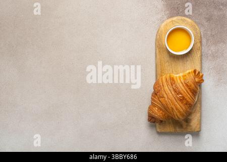 Frisch gebackenes Croissant mit Honig auf Holzbrett in minimalistischer Atmosphäre Stockfoto
