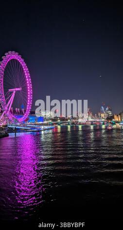 Ein lebhafter nächtlicher Blick auf das London Eye, das in rosa und violetten Tönen beleuchtet ist und sich über die Themse reflektiert. Stockfoto