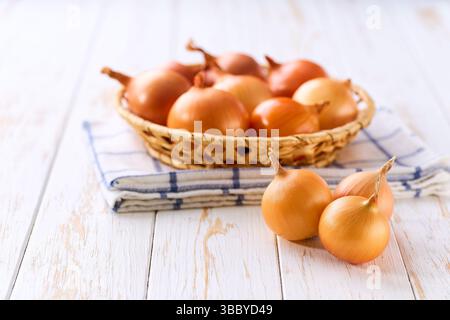 Rohe ganze gelbe Zwiebel in einem Korb auf einem Holztisch, selektiver Fokus. Stockfoto