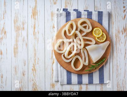 In Scheiben geschnittene Ringe roher Tintenfisch mit Zitrone auf einem weißen Tisch. Draufsicht. Stockfoto