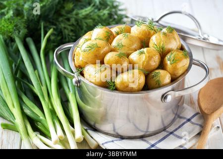 Gekochte junge Kartoffeln mit Butter und frischem Dill auf einem weißen Holztisch, selektiver Fokus. Stockfoto