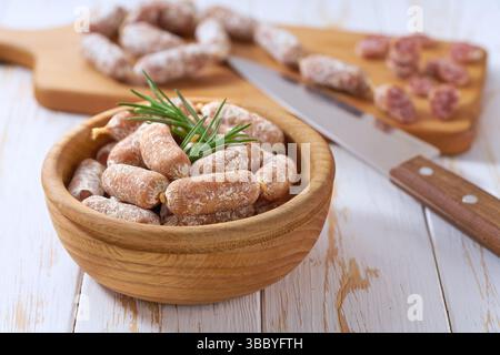Mini Räucherwürste in Holzschale auf einem weißen Holztisch. Mini-Chorizo Stockfoto