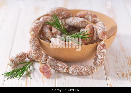 Mini-Salami-Würstchen in einer Schüssel auf einem weißen Holztisch. Stockfoto