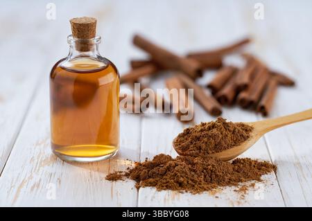 Close Up Flasche Zimtöl mit Zimtstangen und Zimtpulver auf einem weißen Holztisch, gesundes Gewürzkonzept Stockfoto
