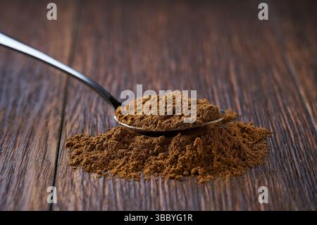 Zimtpulver in einem Metalllöffel auf einem dunklen Holztisch, selektiver Fokus. Stockfoto