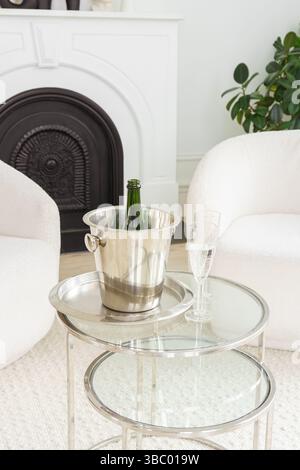Stilvolles Wohnzimmer mit metallischem Eiskübel für Champagner. Zwei elegante Gläser sitzen auf einem Glastisch, bereit für einen festlichen Anlass in modernem W Stockfoto