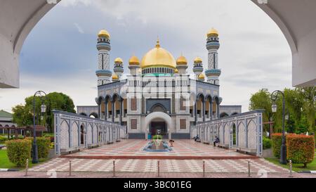 Bandar Seri Begawan, Brunei - 23. Februar 2025: Atemberaubende Architektur der Jame' ASR Hassanil Bolkiah Moschee, eingerahmt von einem Bogen. Die goldene Kuppel glitzert unter einem ruhigen Himmel und schafft eine friedliche Atmosphäre Stockfoto